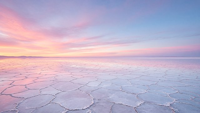 Extremely wide panorama of a white cracked salt flat reflecting a pastel pink and blue dawn sky, original AI device wallpaper